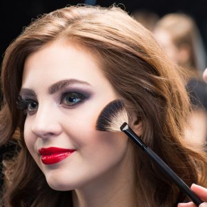 Female make-up artist applying make-up to gorgeous young woman